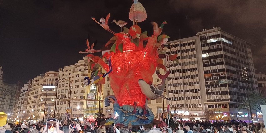 A large crowd is watching a colourful sculpture at night during the Las Fallas festival and enjoying
