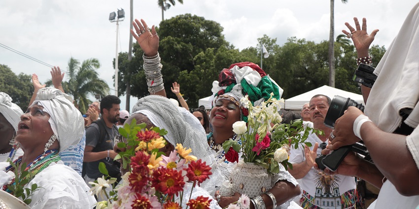 Women dressed in white, wearing jewellery, carrying flower pots, smiling and celebrating