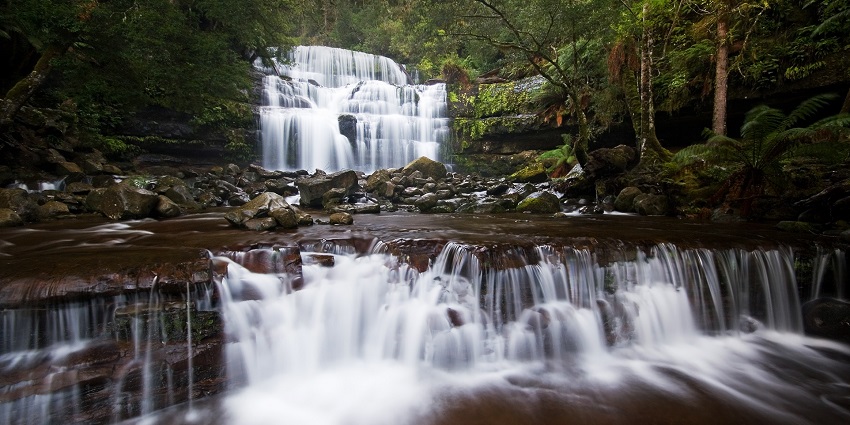 Curtains of water flowing in a layered fashion over rocks, surrounded by the rainforest.