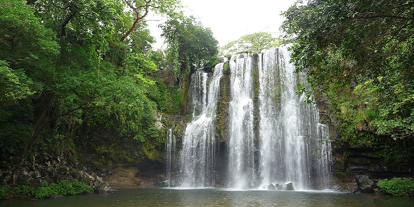Wide view of Llanos de Cortes Waterfall with curtain-like water cascading down rocks.