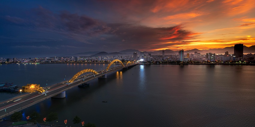 Dragon Bridge in Da Nang illuminated with vibrant yellow lights at night, reflecting on the Han River.