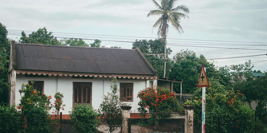 A scenic view of Buon Ma Thuot with a bungalow near coconut trees.