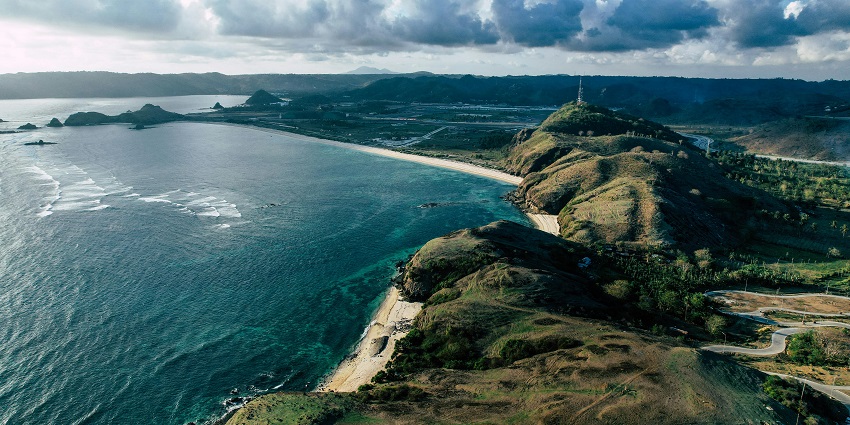 View of places to visit near Bali, Mount Rinjani towering over lush green hills in a Lombok landscape.