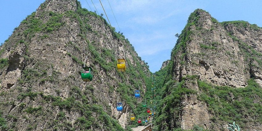 Scenic view of Longqing Gorge with a cable car and sightseeing boat on the river.
