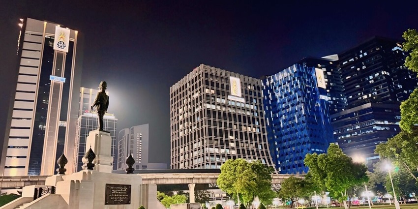 A well-lit nightlife view of tall buildings from a lush green park in Bangkok