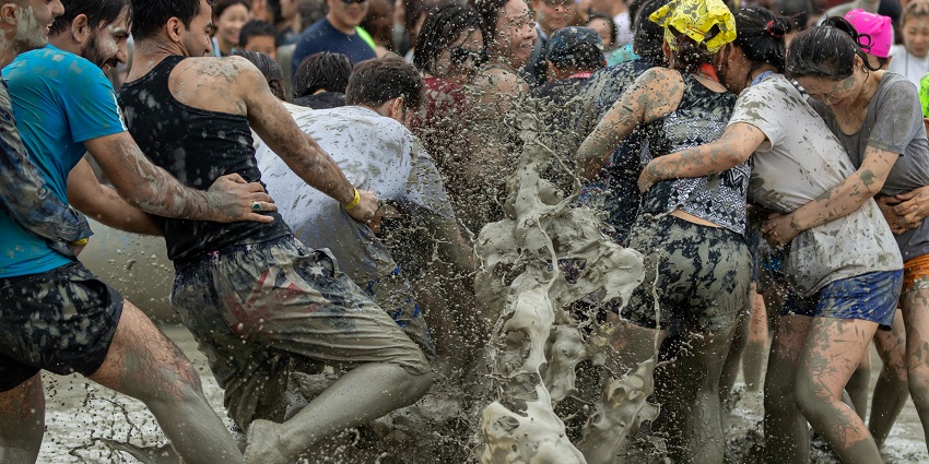 People covered in mud wrestling in the mud pit with one pushing down the other