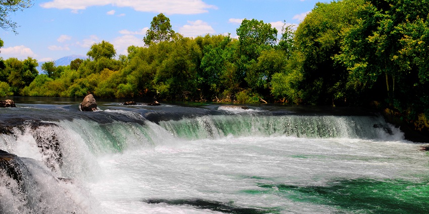 Manavgat waterfall flows downstream into the pool and is surrounded by greenery.