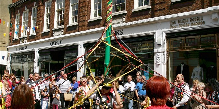 A crowd gathered around a group of people dressed in traditional attire dancing around a Maypole