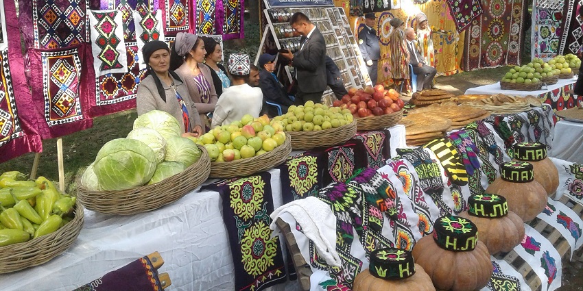 People on stalls with vegetables, fruits and handcrafted clothing outside on a table