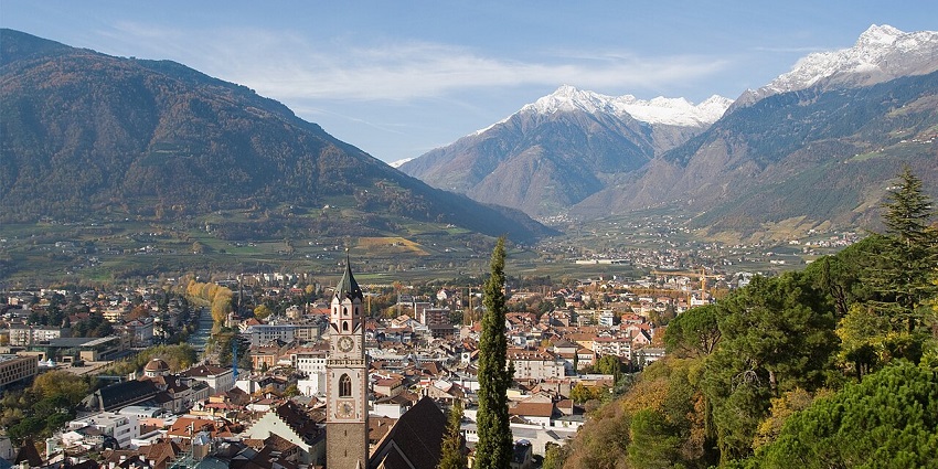 Merano valley with a clock tower, distant houses, buildings and snowy mountain peaks