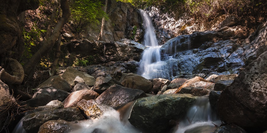 A serene waterfall pool with white water cascading over layered rocky formations.