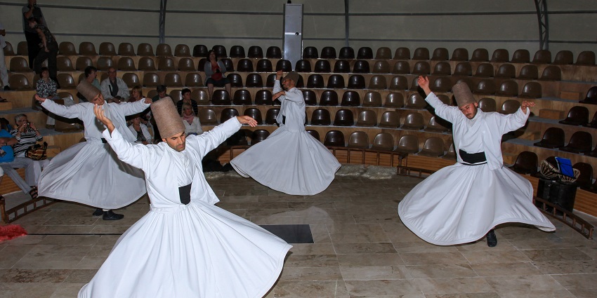 Dervishes are dancing with their hands projected upward, wearing a traditional white dress