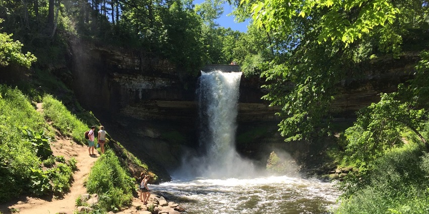 Minnehaha Falls with sunlight highlighting the greenery and people standing nearby