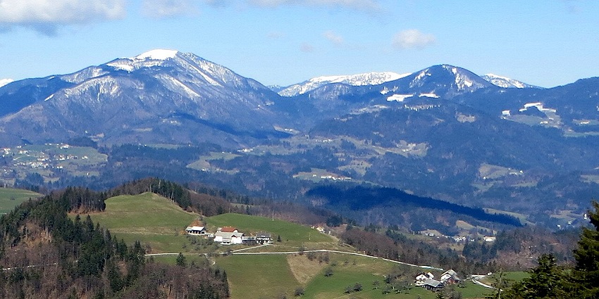 The beautiful scenery of a hill station with small huts and greenery surrounded by snow-clad mountains.