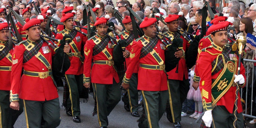 Men parading in red and green clothes with instruments on their shoulders, and other people