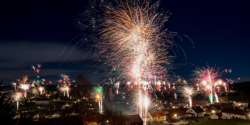 Many firecrackers in flower shapes burn and light up the blue and black night sky