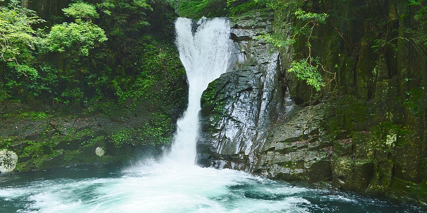 White water cascaded down Nunobiki Falls into a serene bluish pool surrounded by rocks