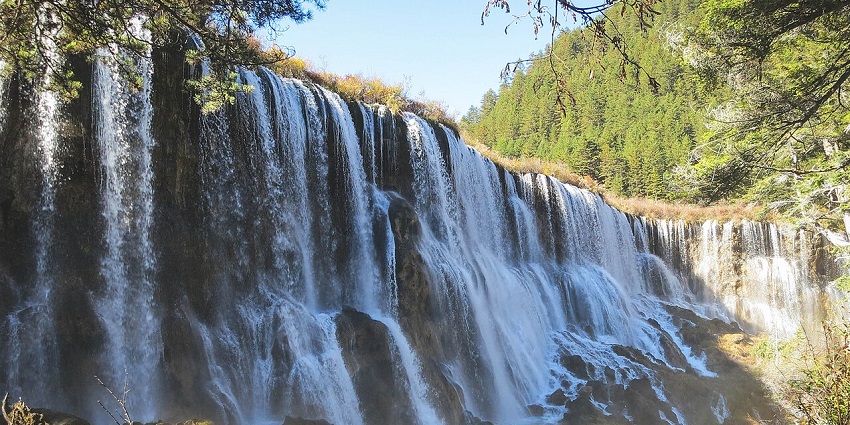 Large Nuorilang Waterfall pours down through rocky tiers in a scenic green landscape.