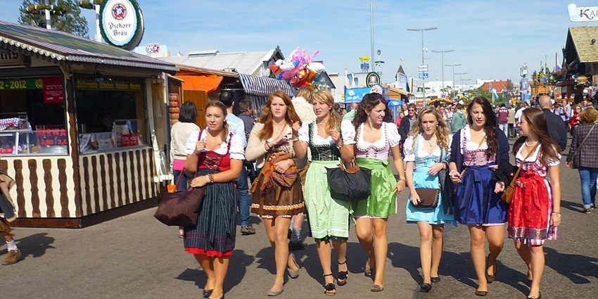 A group of women walking around in costumes of dirndls, aprons and carrying side bags