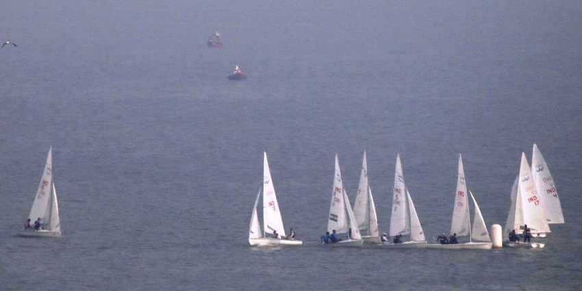 A traditional boat race with sailors competing in calm waters under a misty sky.