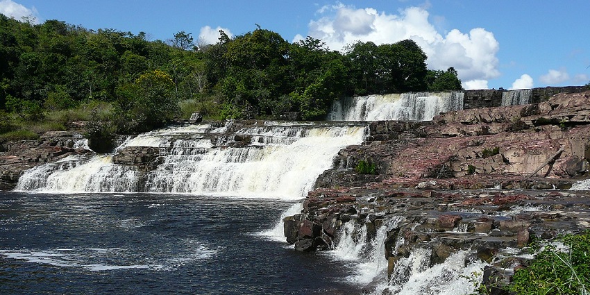 Orinduik Falls flowing over jasper rocks with lush greenery and a clear blue sky above