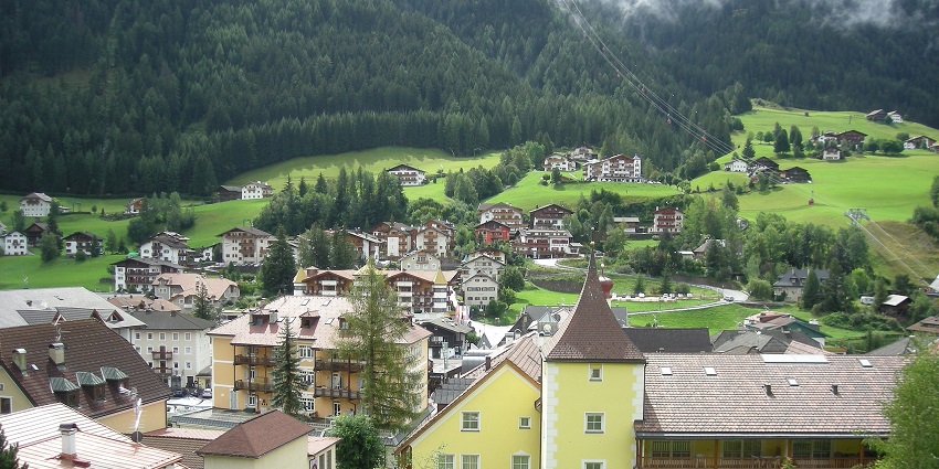 Ortisei with multiple town buildings surrounded by greenery and mountains with misty peaks