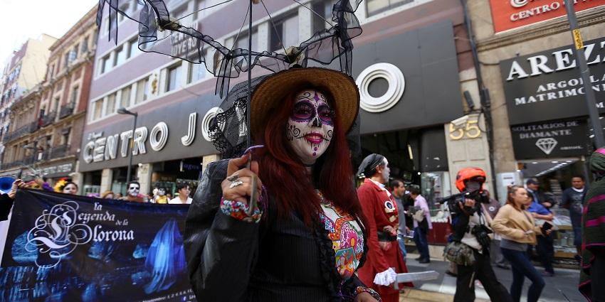 A person carrying a fancy umbrella in a costume and smiling with a painted face