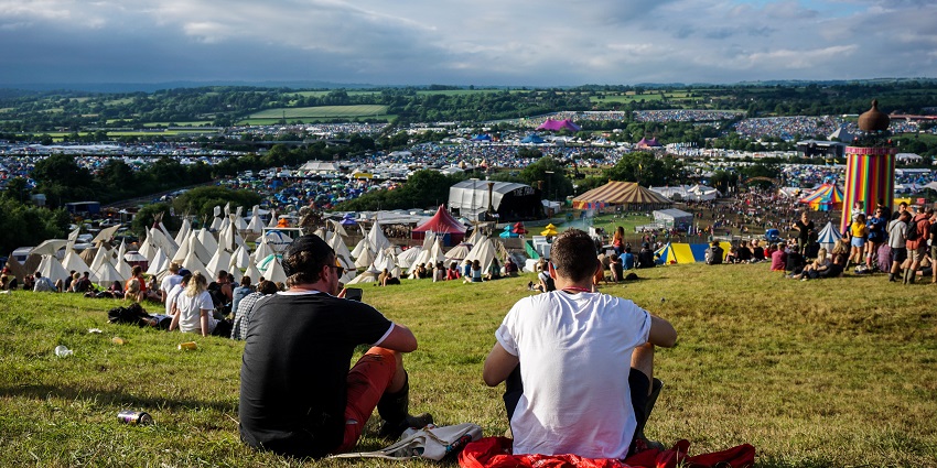 Two men sitting on the highest point of the farm at Glastonbury Festival with an ongoing fest