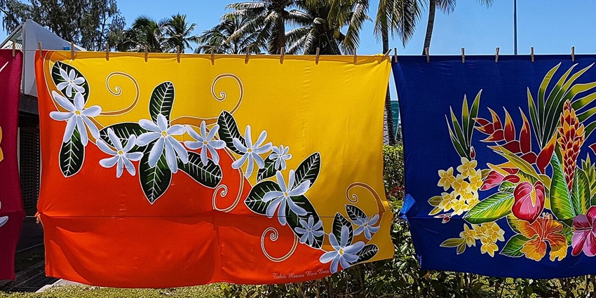 A display of colorful pareos (sarongs) hanging on a clothesline, showing vibrant patterns and tropical designs.