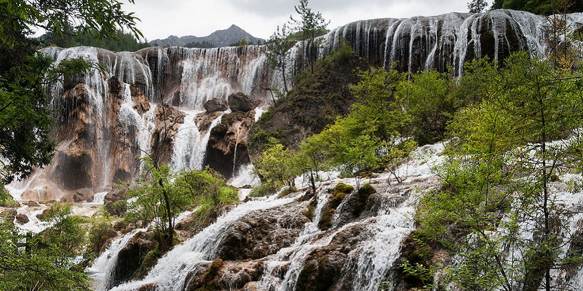 Multi-layered silver-coloured water cascades through rocks surrounded by greenery.