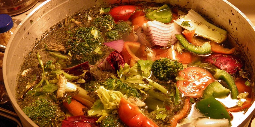 Image of a steaming bowl of soup, resembling the Pepper Pot Soup with callaloo and chunks of yam.