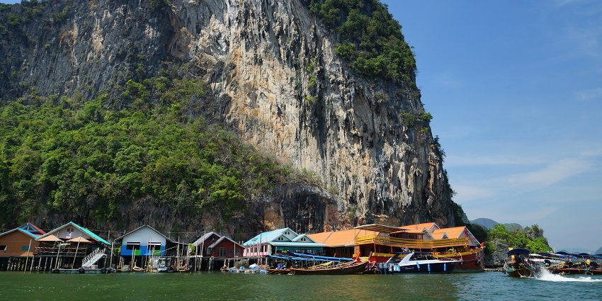 Image of a group of houses sitting on top of a lush green hillside - a timleless Sea Gypsy Village in Phang Nga Bay