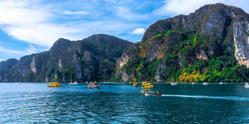 Clear turquoise waters and sandy beach at Phi Phi Islands with distant cliffs.