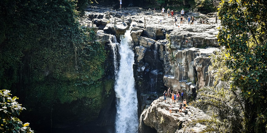Beautiful cascading waterfall flowing over rocks into a turquoise pool surrounded by trees.
