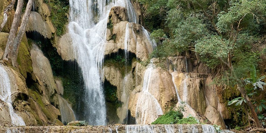 The Ponot waterfall in a tropical area, with crystal-clear water flowing over rocky cliffs.