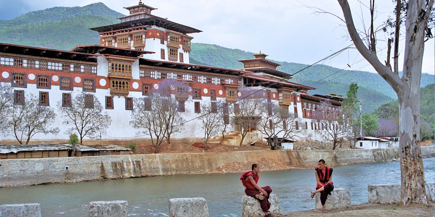 An image of Punakha temple in Bhutan with hills in the background and two monks sitting outside.