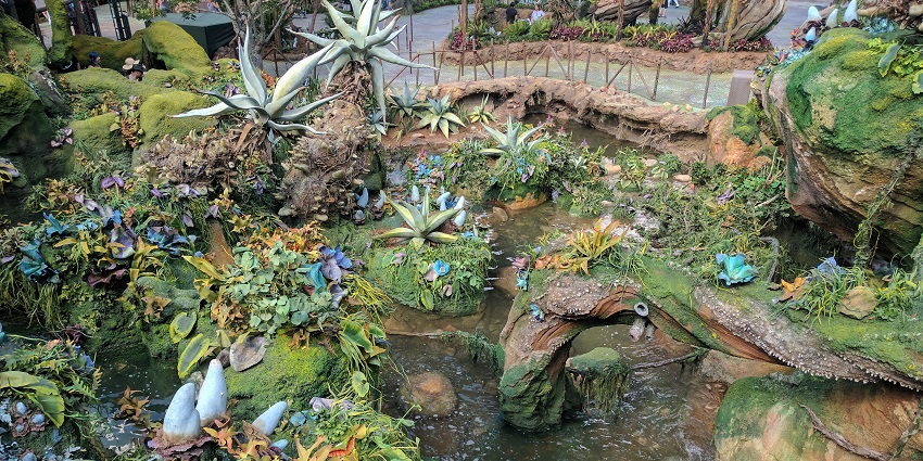 People bathing in a natural waterfall pool surrounded by rocks and lush greenery.