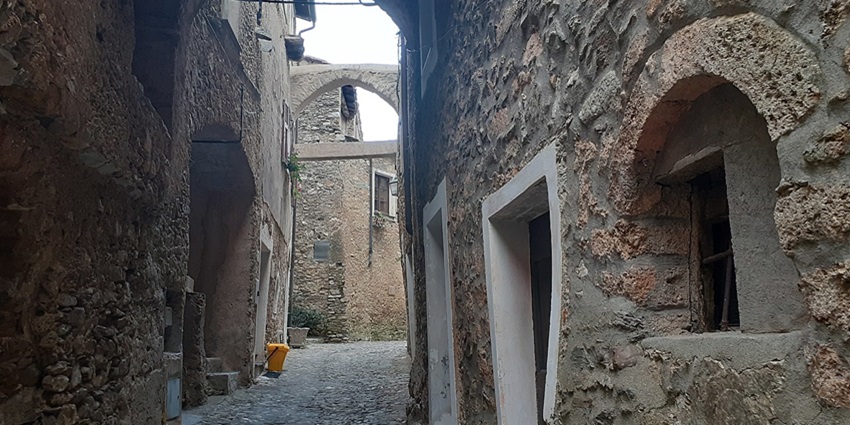 Shadowed narrow alleys with stone walls and hanging signs, exploring Caruggi is an old-world thing to do in Genoa.