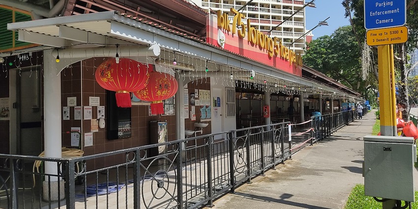 People queue and dine at a busy hawker centre in Toa Payoh, surrounded by food stalls.