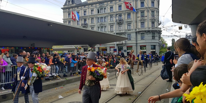 People in traditional Swiss costumes parade with flowers during a spring festival.
