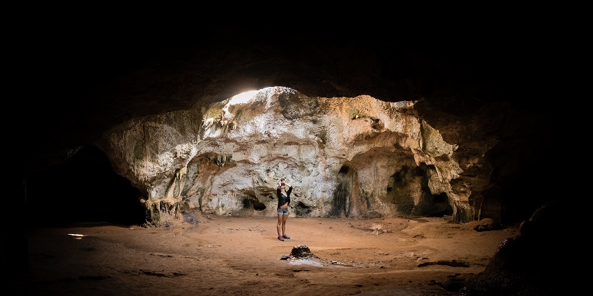 An image of a small cave opening at one of the Aruba caves with a tourist standing.