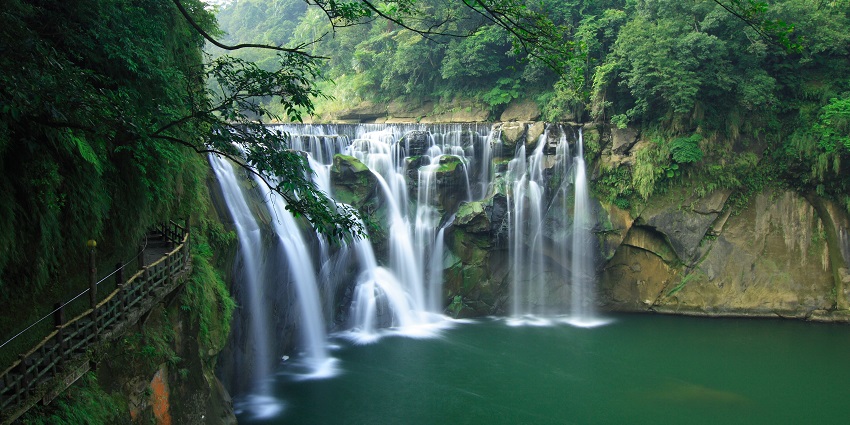 A serene waterfall tumbles down a rugged cliffside, surrounded by lush green foliage.