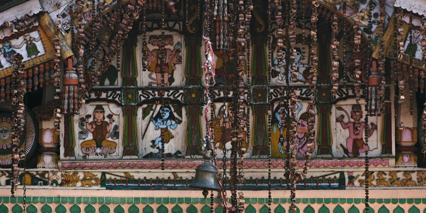Hindu deity sculpture with bell at Hanol temple, showcasing detailed carvings and vibrant