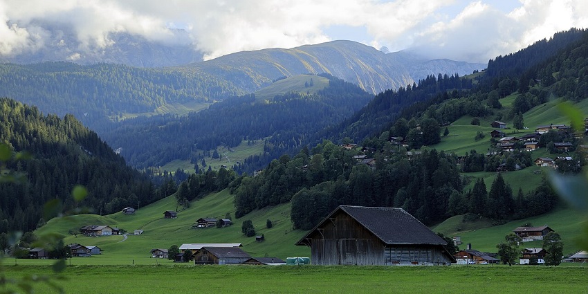 Simmental Valley with scattered village houses, greenery, and alpine trees in valleys in Switzerland.