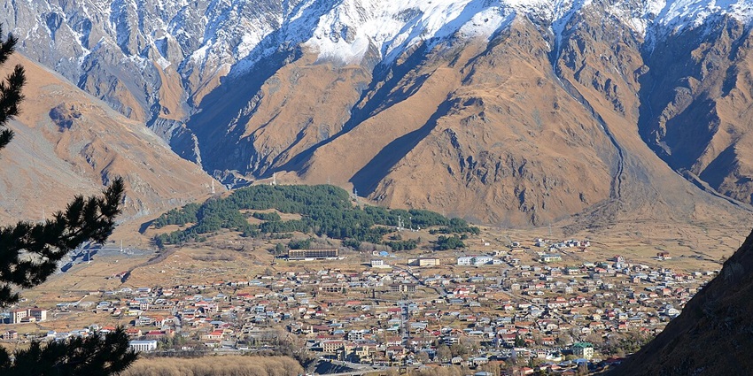 Mountain town with buildings, trees, and scenic views, all around one of the calmest things to do in Kazbegi.
