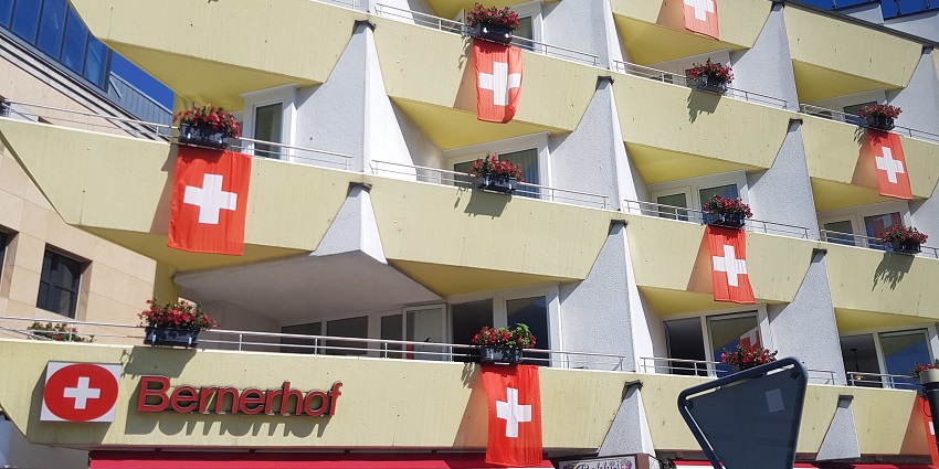 Swiss national flags hanging from balconies of apartment buildings during celebration.