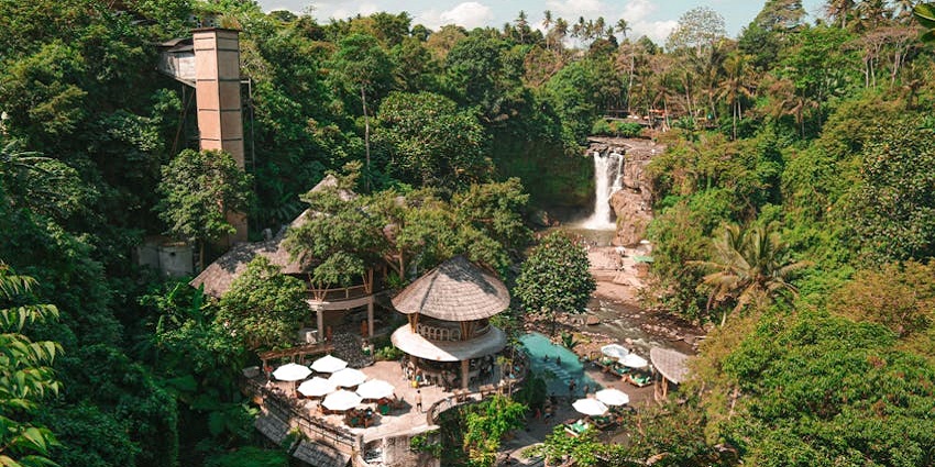 A view of Tegenungan Waterfall with water cascading down a cliff, surrounded by green jungle.