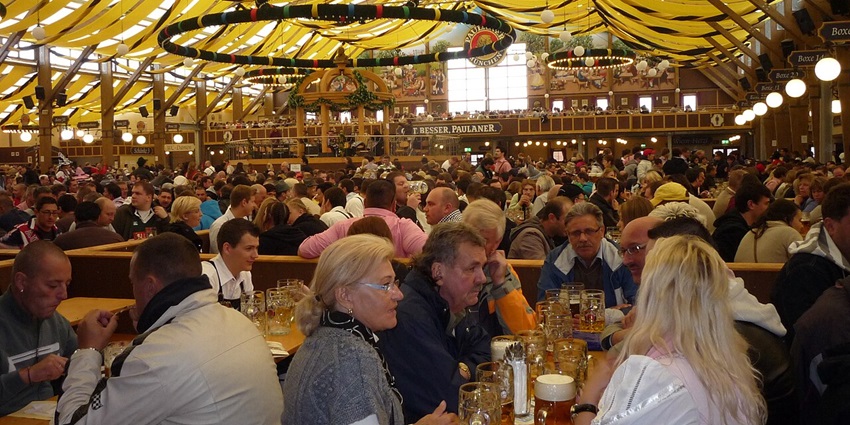 A tent in oktober festival with a well decorated roof, hanging lights and a lot of people sitting
