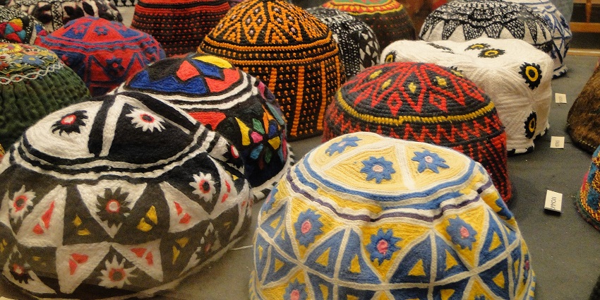 Beautifully embroidered Omani kummahs in various colours, neatly arranged in a market stall, things to buy in Oman.