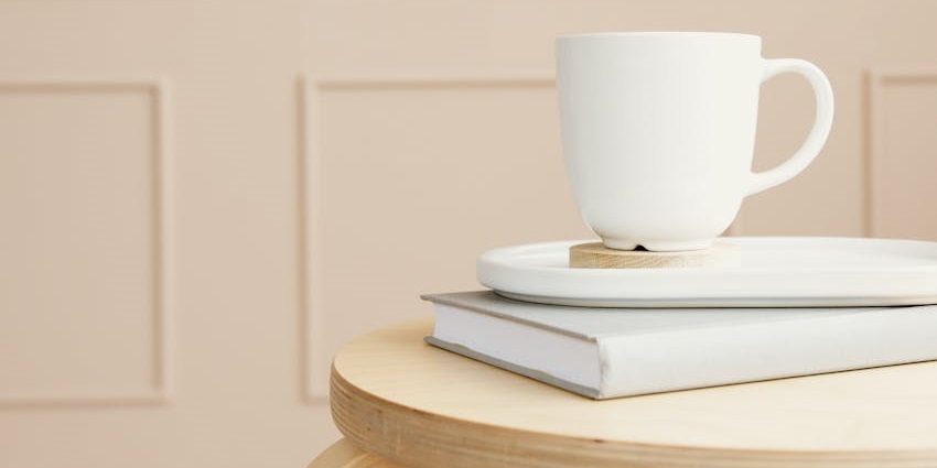 White ceramic mug on a tray with a book, set on a wooden table with light–things to buy in thailand